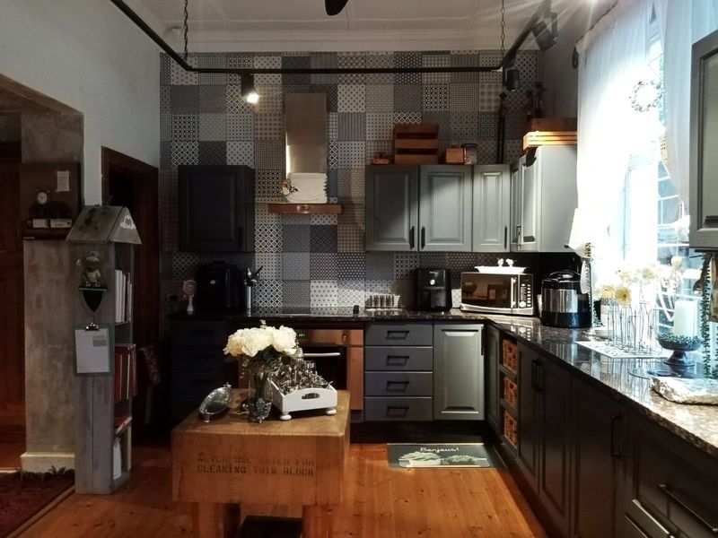 A well-appointed kitchen featuring dark cabinetry, stone countertops, a striking patterned tile splashback, built-in oven, and warm timber flooring.