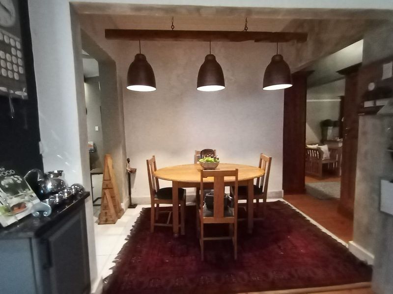 A cozy dining area featuring a round table set under three industrial-style pendant lights suspended from a rustic timber beam.