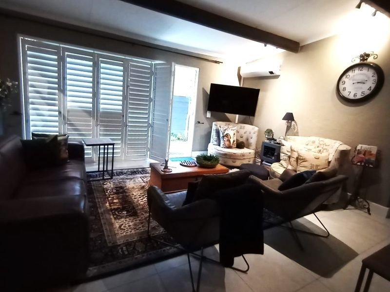A comfortable living room featuring tiled flooring, an exposed ceiling beam, and plantation shutters opening to the exterior.
