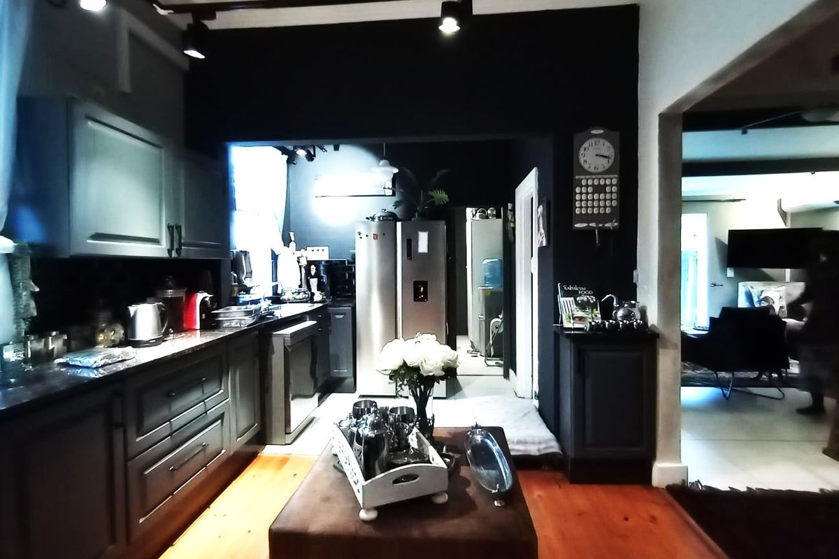 A modern kitchen featuring dark cabinetry, granite countertops, and track lighting, with warm hardwood flooring and an open flow into the adjacent living area.