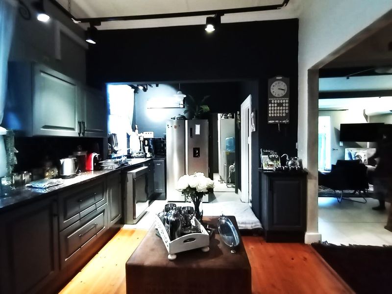 A modern kitchen featuring dark cabinetry, granite countertops, and track lighting, with warm hardwood flooring and an open flow into the adjacent living area.