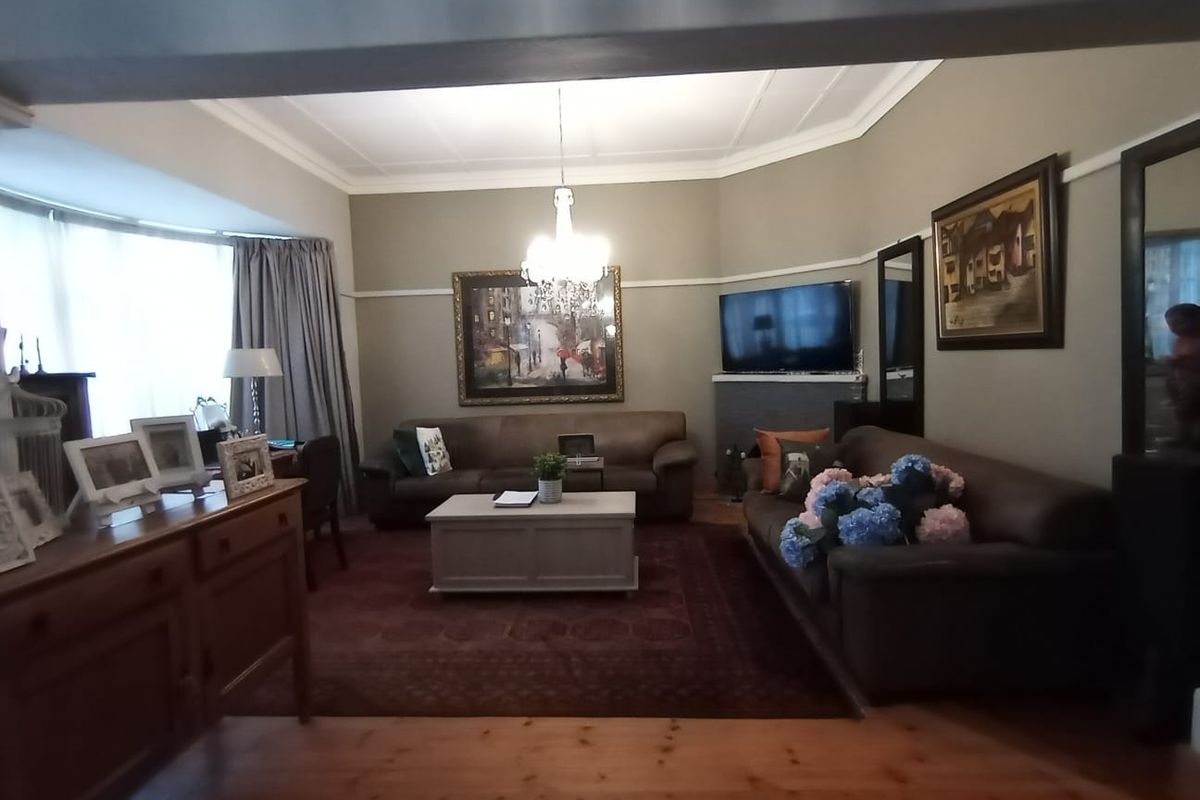 A comfortable living room featuring timber flooring, a bay window, and classic architectural details including picture rails and a ceiling rose.