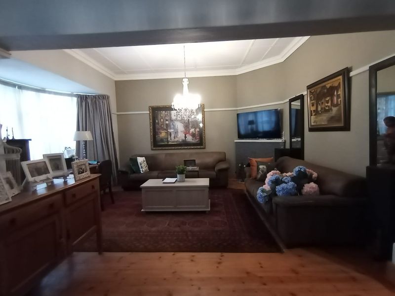 A comfortable living room featuring timber flooring, a bay window, and classic architectural details including picture rails and a ceiling rose.