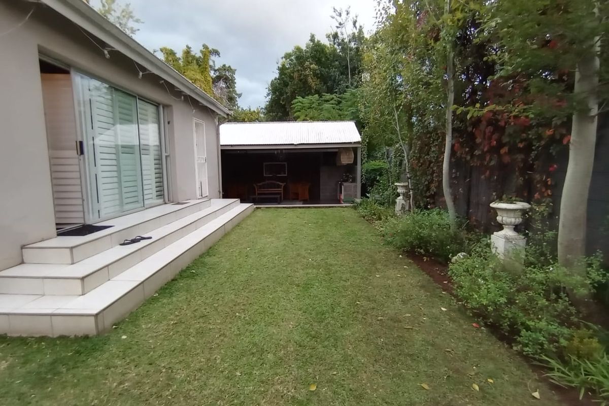 Rear garden view featuring a lawn, tiled patio steps leading to sliding glass doors, and a detached outbuilding with a corrugated metal roof.