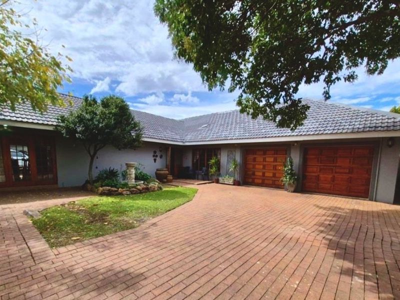 Front exterior view of the property featuring a brick paved driveway, double garage with wooden doors, and a landscaped garden area with a water feature.