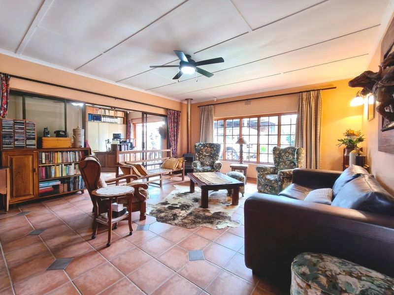 Spacious living room featuring tiled flooring, a wood-burning fireplace, ceiling fan, and large windows providing natural light and access to the adjacent area.