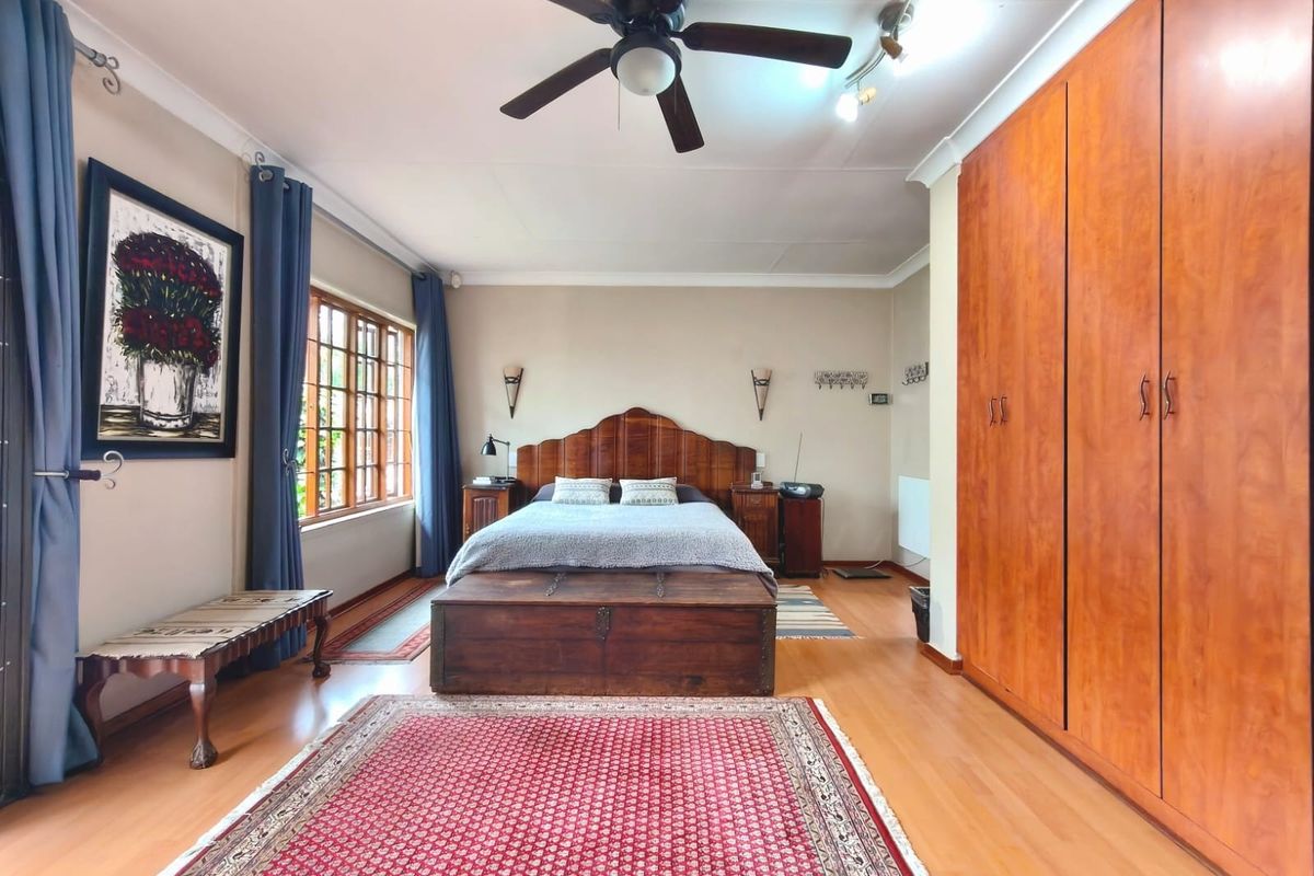Spacious bedroom featuring warm laminate flooring, extensive built-in wooden cabinetry, a ceiling fan, and large windows allowing for natural light.