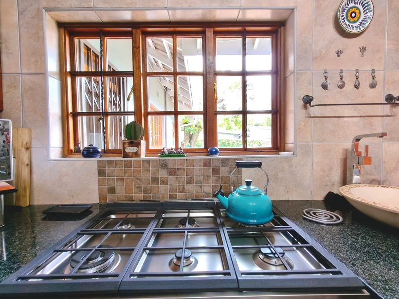 A well-maintained kitchen area featuring a built-in gas hob, granite countertops, and a tiled backsplash with a view through a wooden window.