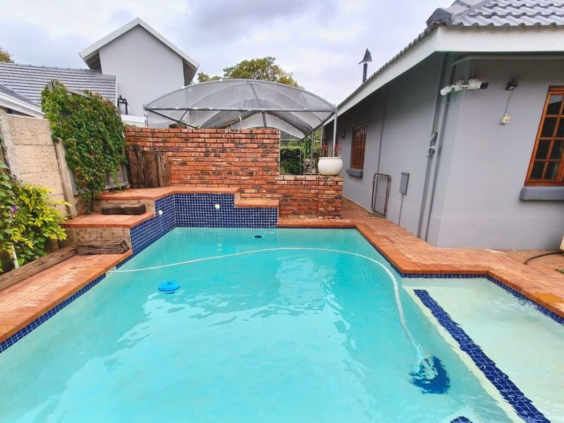 A private swimming pool area featuring a brick retaining wall, tiled coping, and an adjacent outdoor gazebo structure.