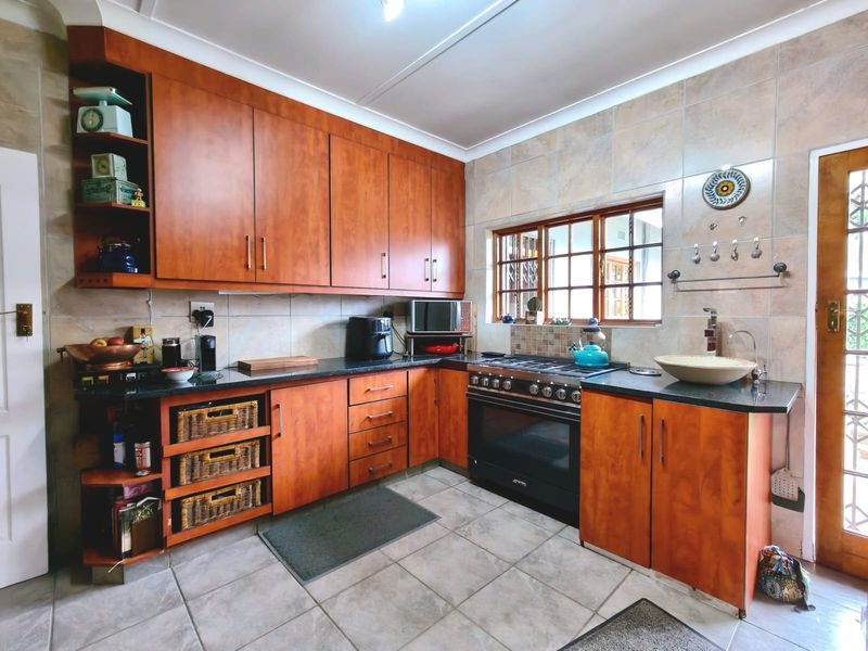 A functional kitchen featuring warm-toned wooden cabinetry, granite countertops, a gas stove with oven, and tiled finishes throughout.