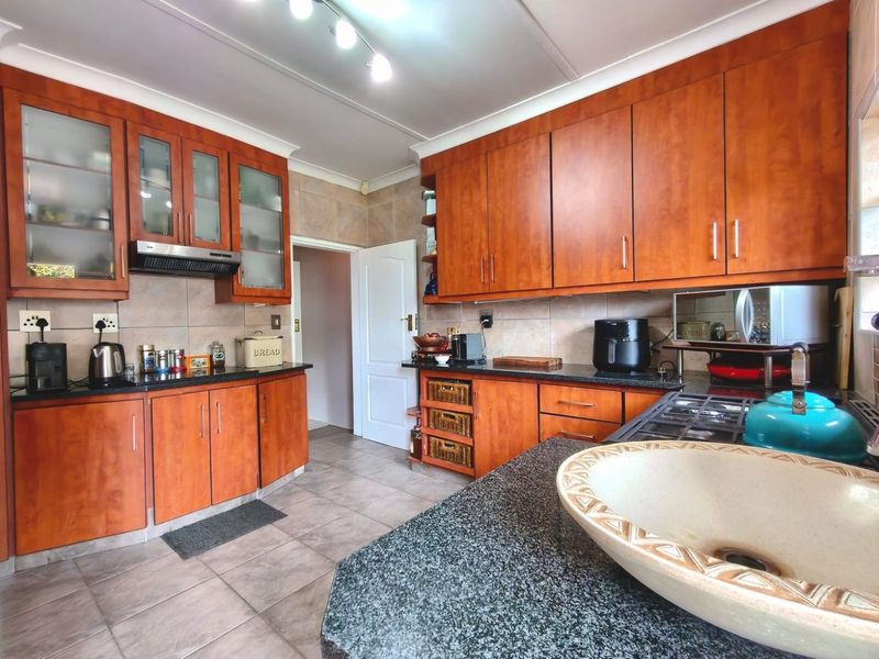 A functional kitchen featuring warm-toned wooden cabinetry, granite countertops, tiled flooring, and a tiled backsplash, offering ample storage and workspace.