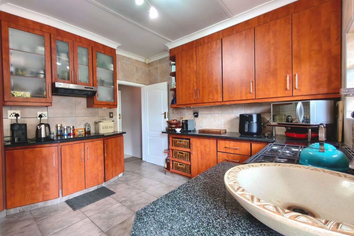 A functional kitchen featuring warm-toned wooden cabinetry, granite countertops, tiled flooring, and a tiled backsplash, offering ample storage and workspace.