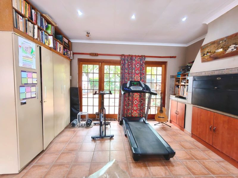 A multi-purpose living space featuring built-in cabinetry, a fireplace, tiled flooring, and direct access to the garden through wooden french doors.