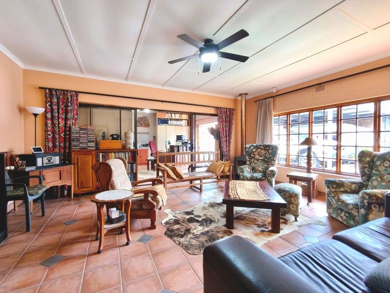 Spacious living room featuring terracotta tiled flooring, a wood-burning stove, ceiling fan, and large windows providing ample natural light.