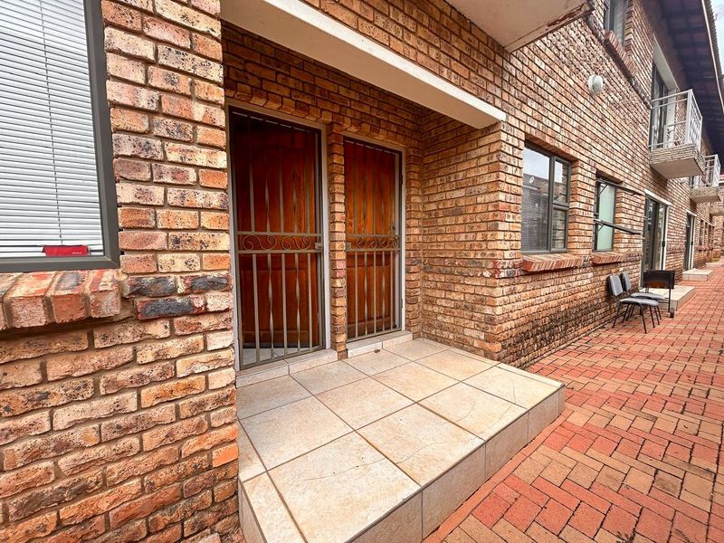 Exterior view of an apartment entrance featuring a face brick facade, tiled porch area, and secure metal gate access.