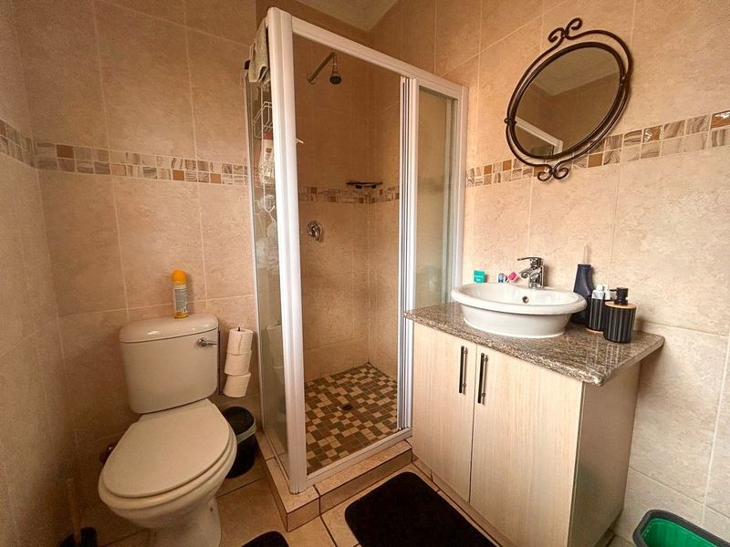 A functional bathroom featuring a shower enclosure, vanity cabinet with granite countertop, vessel sink, and neutral wall tiling.