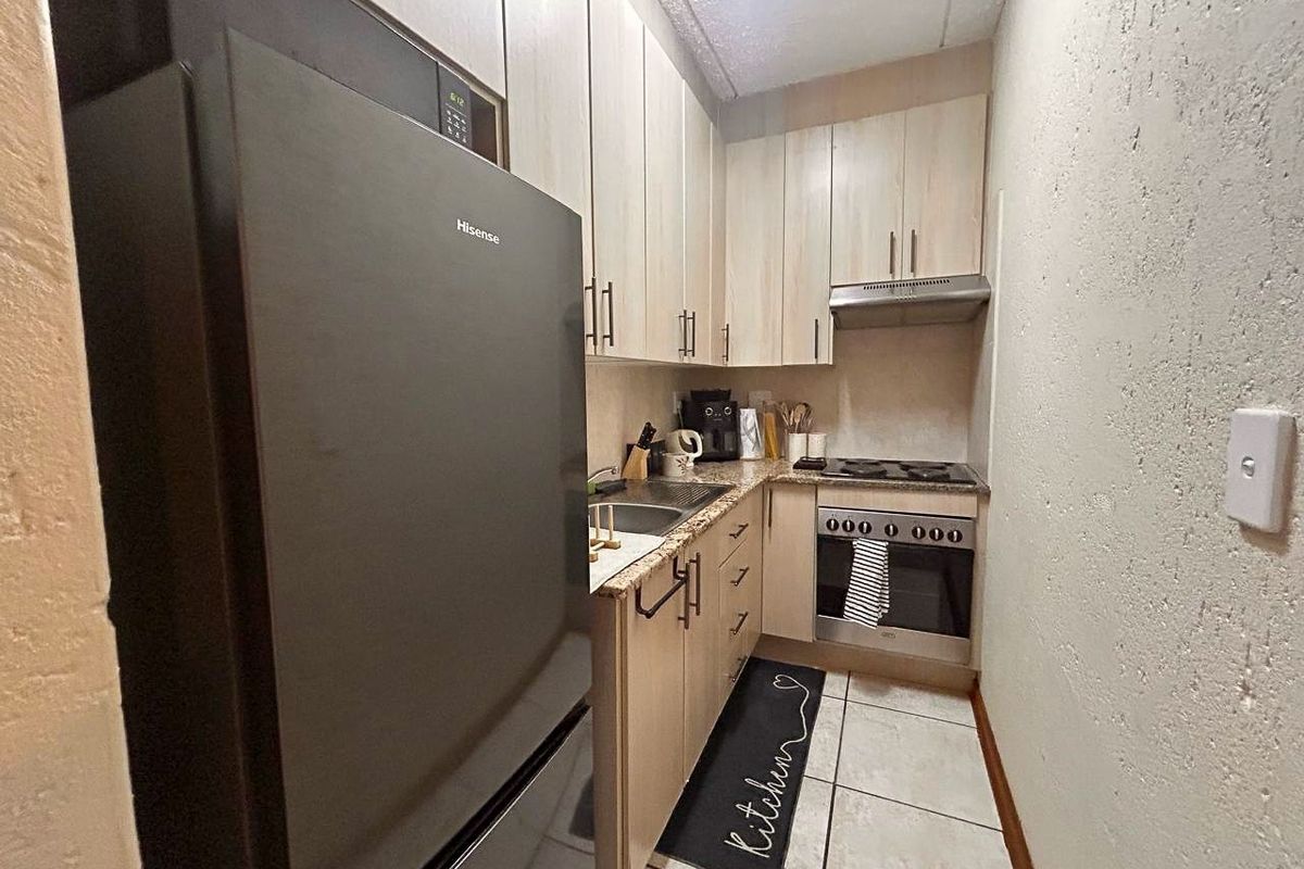 Compact galley-style kitchen featuring light wood-finish cabinetry, granite countertops, integrated oven, and hob with an overhead extractor fan.