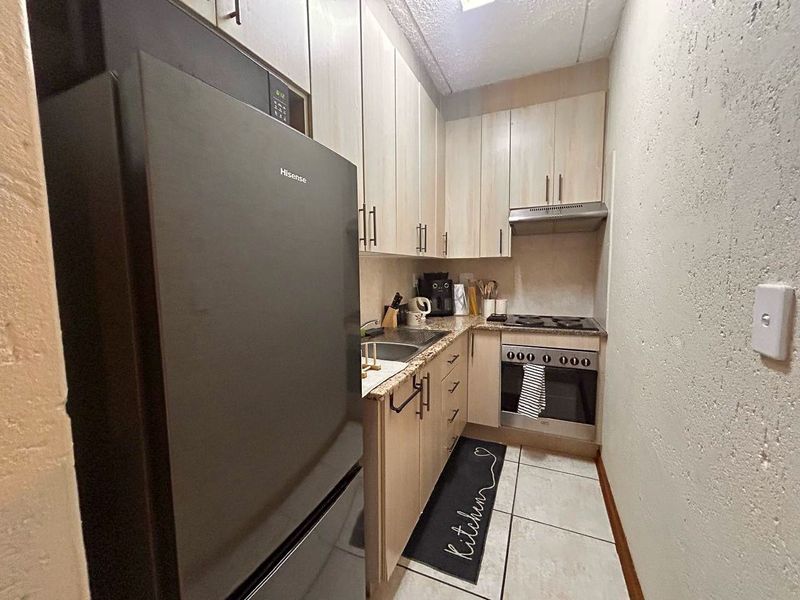 Compact galley-style kitchen featuring light wood-finish cabinetry, granite countertops, integrated oven, and hob with an overhead extractor fan.