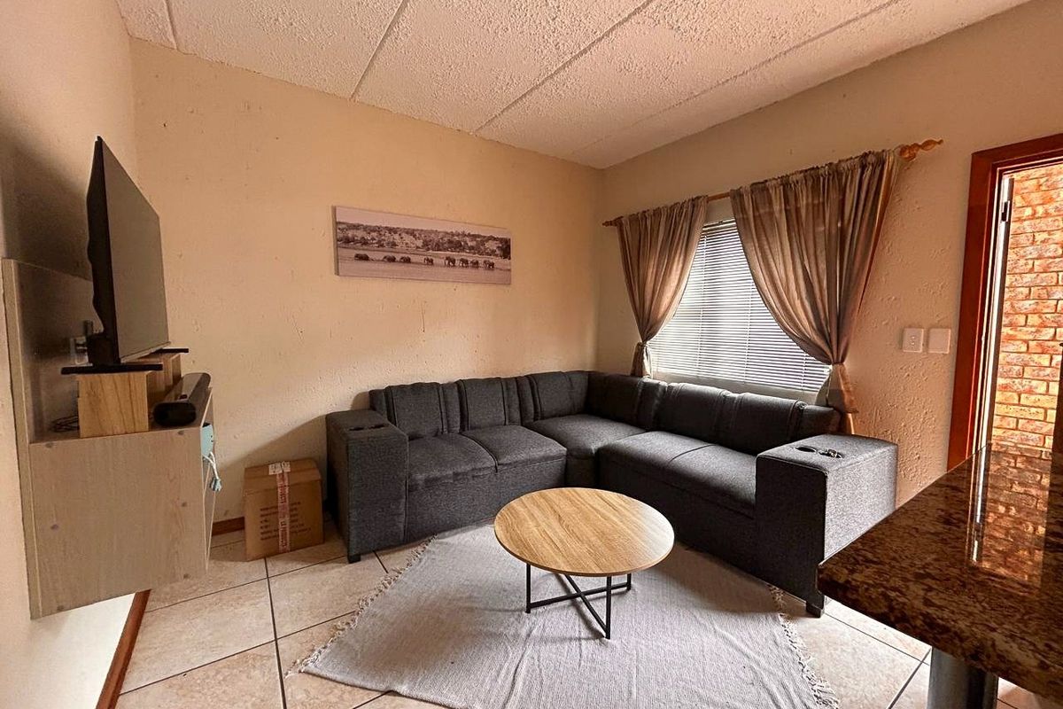 A compact living room featuring tiled flooring and a textured ceiling, providing a functional space with natural light from the window.