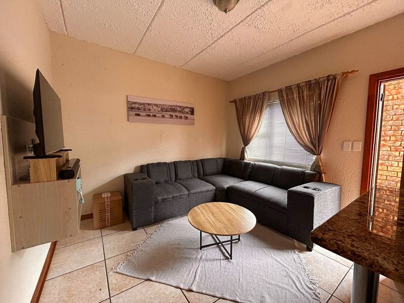 A compact living room featuring tiled flooring and a textured ceiling, providing a functional space with natural light from the window.