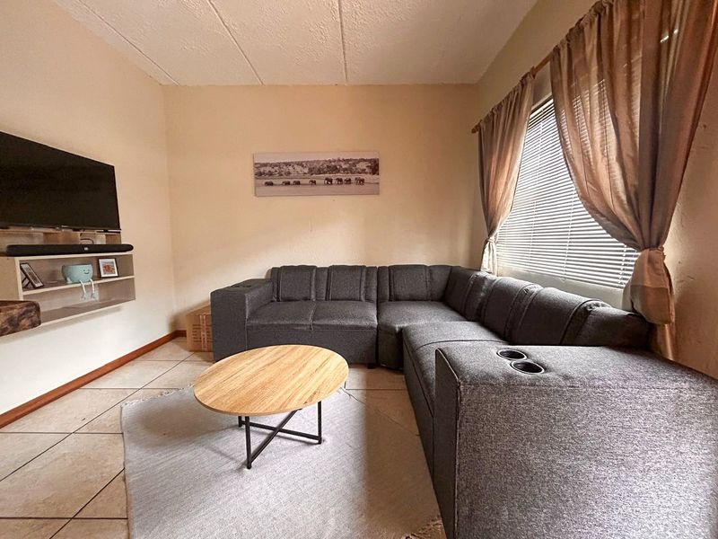 A comfortable living room featuring tiled flooring, textured ceilings, and venetian blinds, providing a functional and neutral space for relaxation.