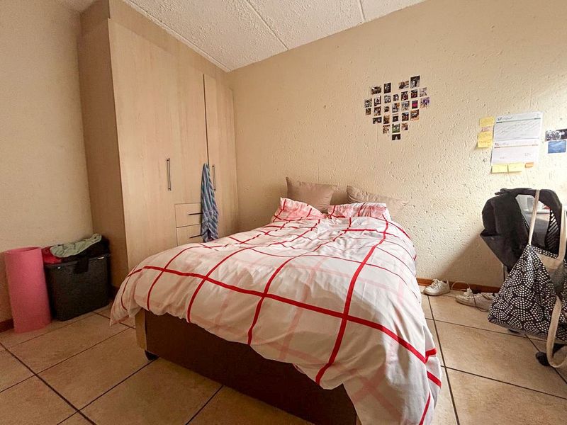 A bedroom featuring built-in wardrobes, tiled flooring, and textured wall finishes, offering a functional space with potential for cosmetic updates.