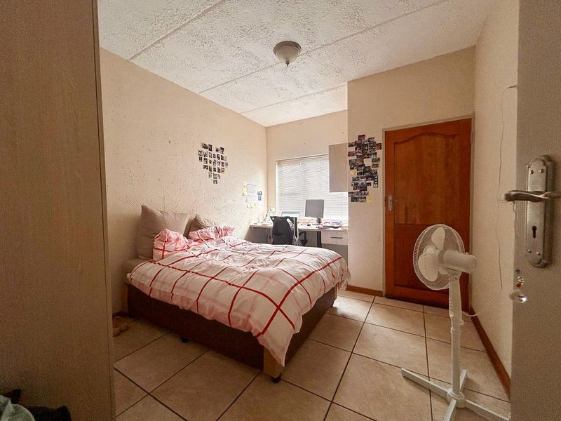 A compact bedroom featuring tiled flooring, a textured ceiling, and a wooden door, providing a functional space with potential for cosmetic updates.