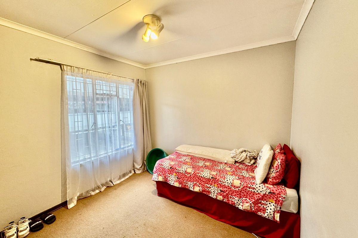 A standard bedroom featuring carpeted flooring, a window with security bars, and a central ceiling light fixture.