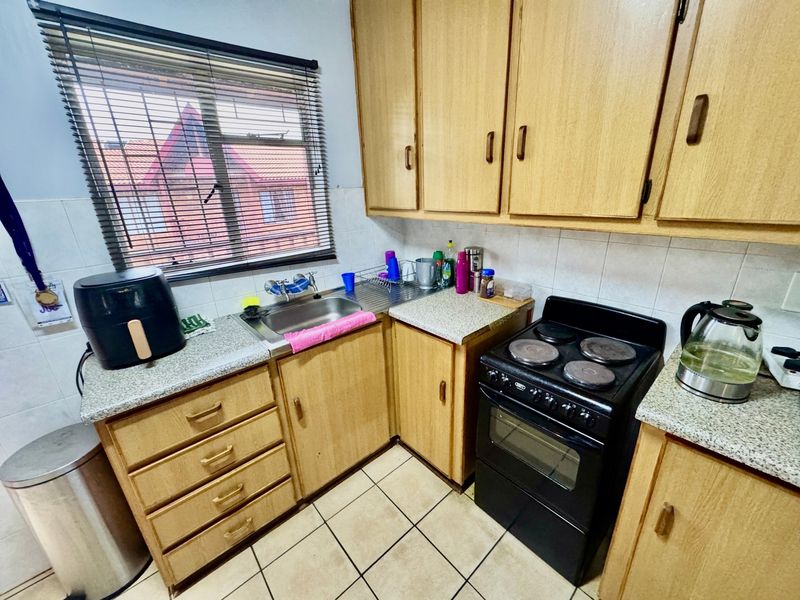 A functional kitchen featuring laminate cabinetry, tiled splashbacks, a stainless steel sink, and a freestanding electric stove with ceramic tile flooring.
