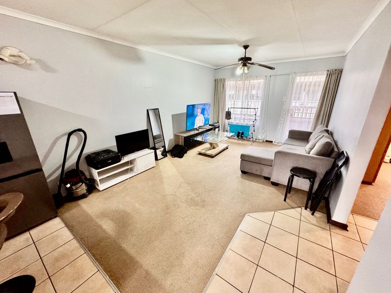 A living room featuring a combination of tiled and carpeted flooring, a ceiling fan, and access to a balcony through sliding glass doors.