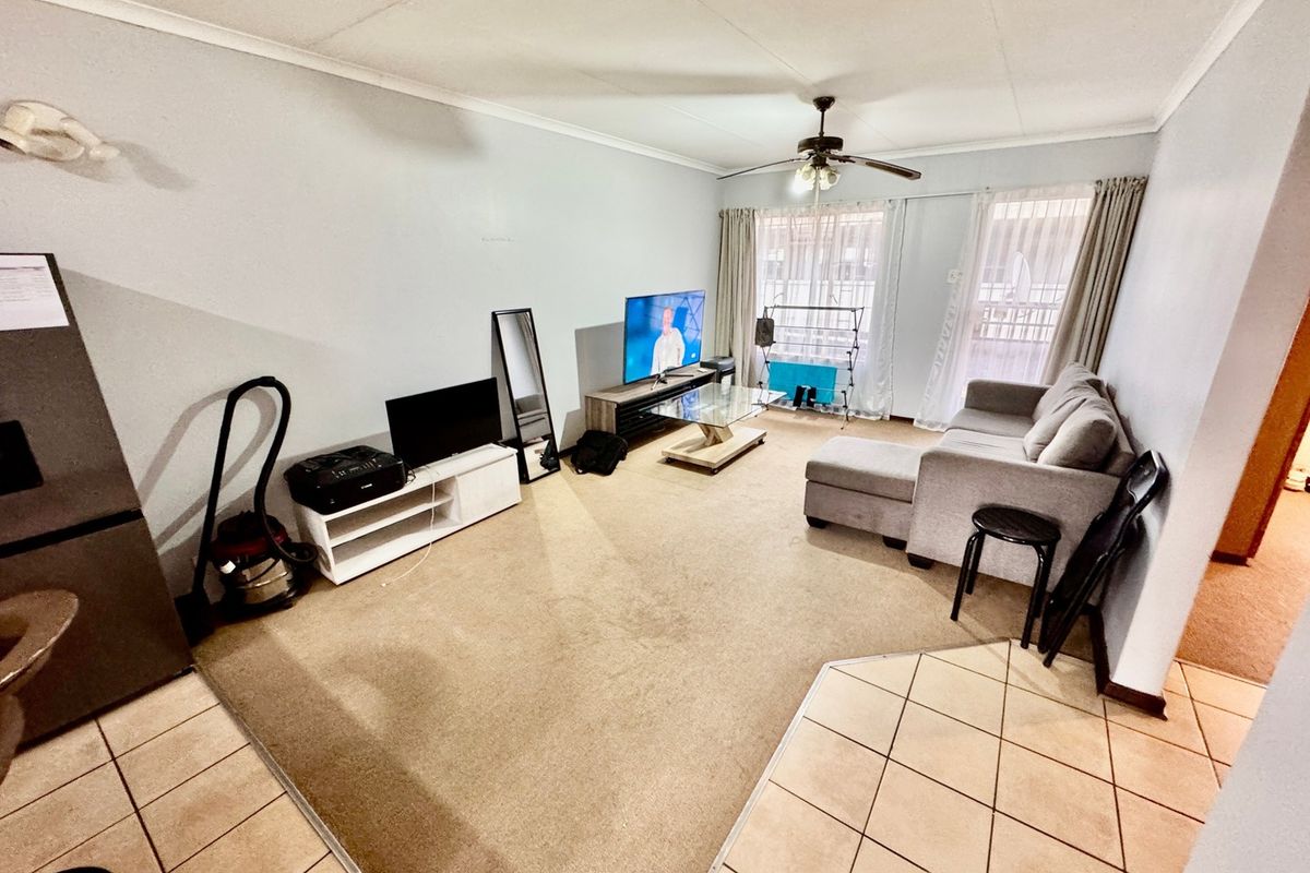 A living room featuring a combination of tiled and carpeted flooring, a ceiling fan, and access to a balcony through sliding glass doors.