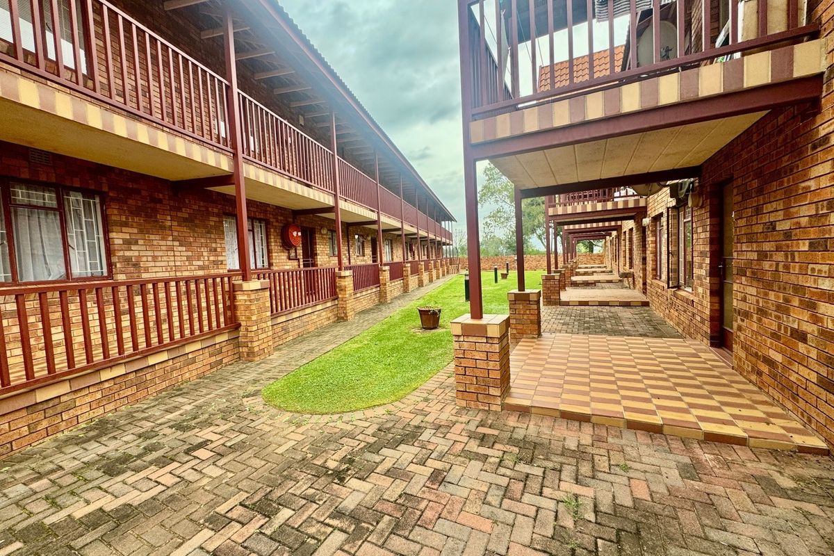 A view of the apartment complex exterior featuring face brick facades, paved courtyard areas, and covered balconies with metal railings.