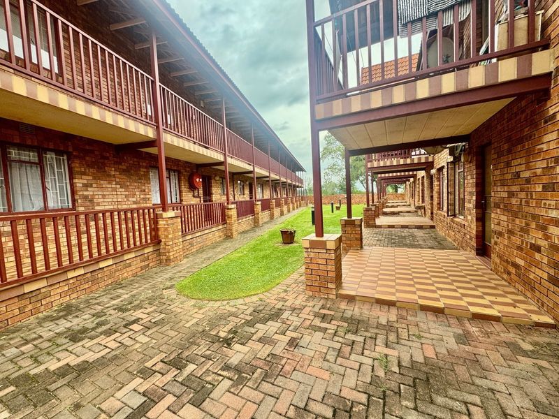A view of the apartment complex exterior featuring face brick facades, paved courtyard areas, and covered balconies with metal railings.