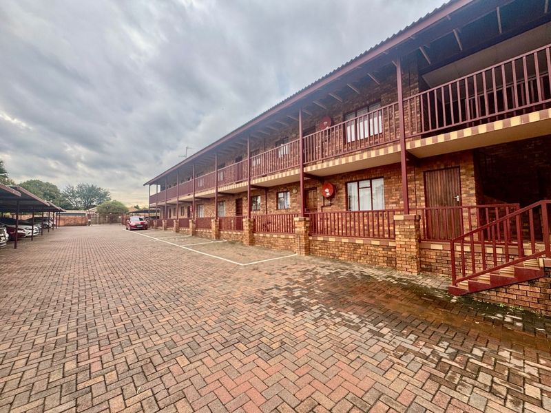 Exterior view of a multi-story apartment complex featuring face brick construction, covered parking bays, and accessible balcony walkways.