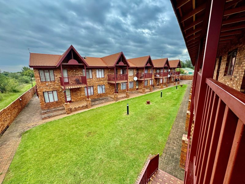 A view of the apartment complex exterior featuring face brick facades, tiled roofs, private balconies, and a well-maintained communal lawn area.