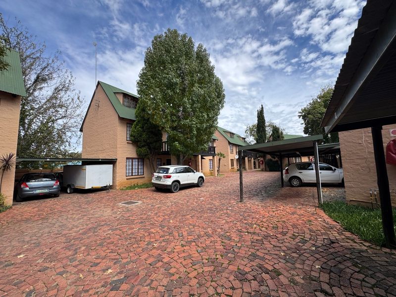 Exterior view of an apartment complex featuring brick-paved driveway, covered parking carports, and multi-story residential buildings with pitched roofs.