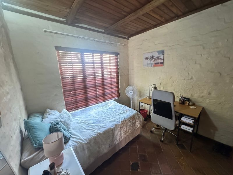 A rustic bedroom featuring exposed timber ceiling beams, textured stone walls, and terracotta floor tiles, offering a unique character-filled living space.