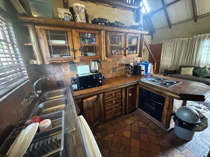 Rustic kitchen featuring wooden cabinetry, stone tile backsplash, terracotta flooring, and exposed timber beams, offering a warm, traditional aesthetic.
