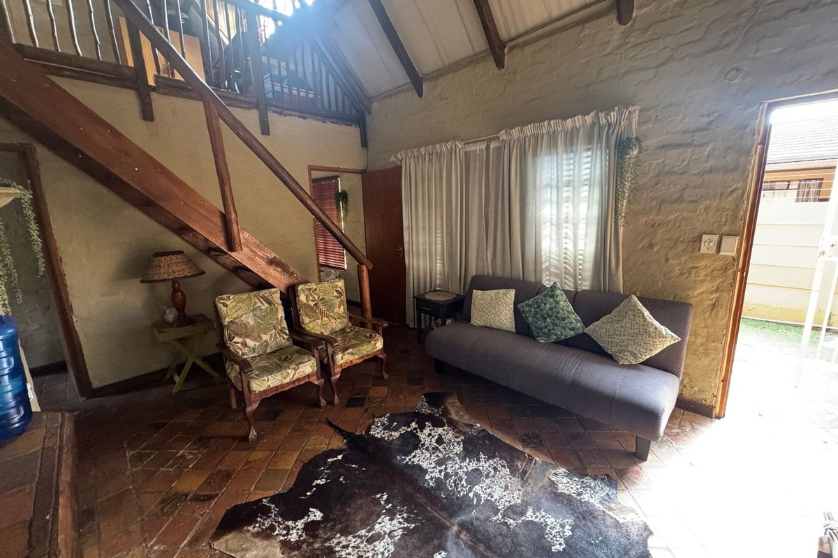 Rustic living room featuring exposed timber beams, a wooden staircase leading to a mezzanine level, and traditional terracotta floor tiles.