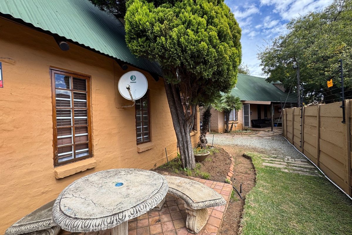 Rear exterior view of the apartment featuring a paved patio area, established garden, and secure perimeter wall with electric fencing.