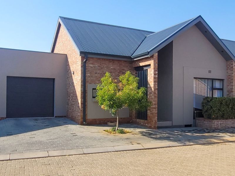 Modern townhouse exterior featuring a brick and plaster facade, metal roof, and a paved driveway leading to a single garage.