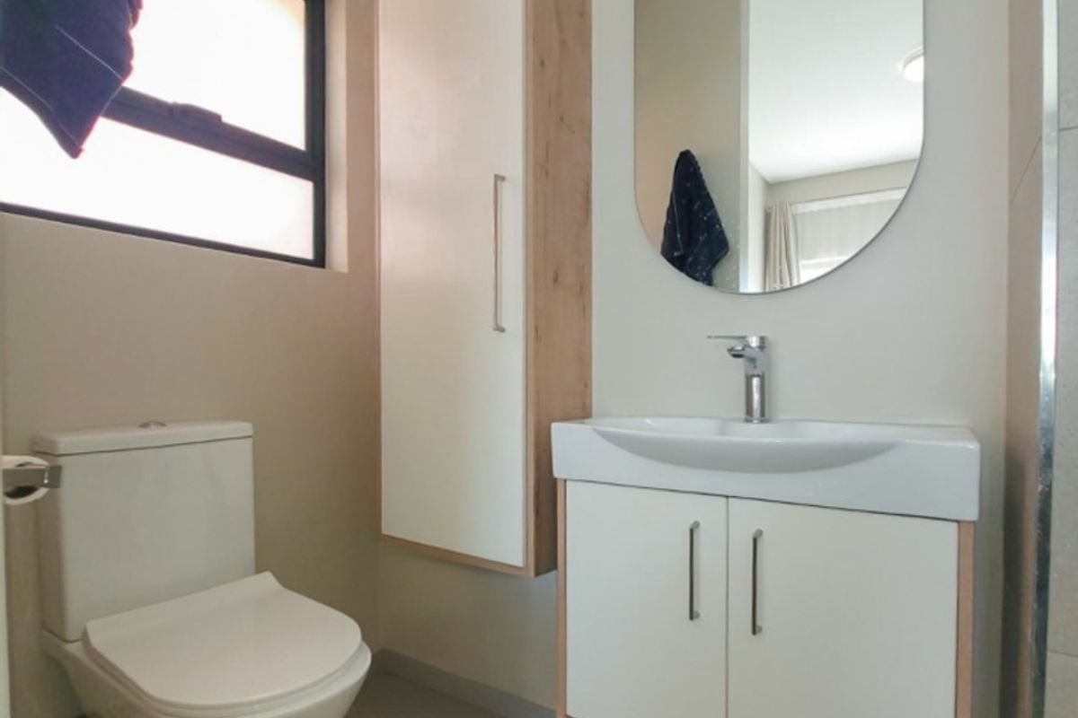 Modern bathroom featuring a wall-mounted vanity with basin, sleek storage cabinet, oval mirror, and a standard toilet with tiled flooring.