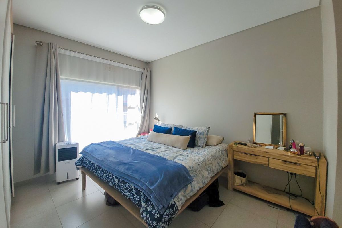 A well-lit bedroom featuring neutral tiled flooring, a built-in cupboard, and a sliding glass door providing natural light.