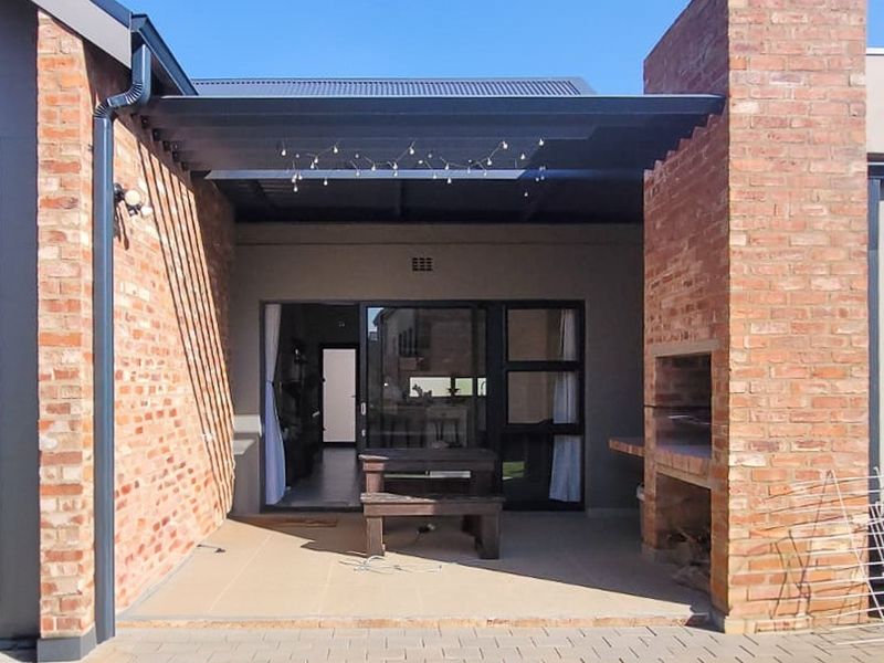 A covered outdoor patio featuring a built-in brick braai, tiled flooring, and direct access to the interior through sliding glass doors.