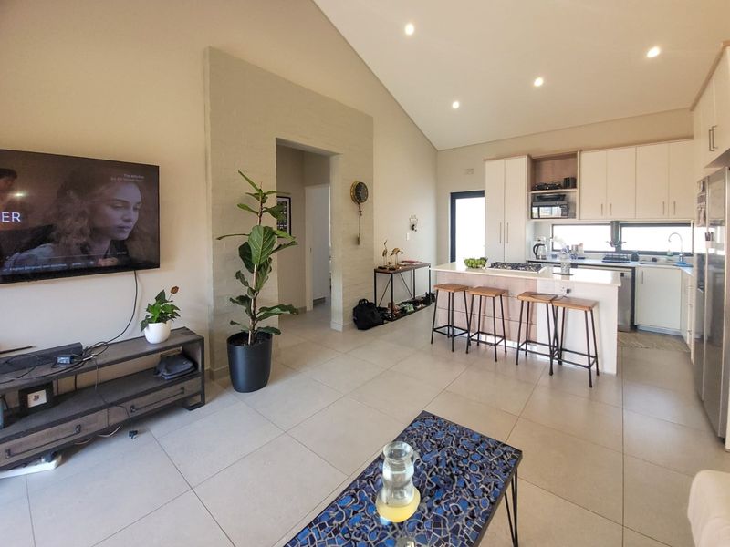 Spacious open-plan living area featuring a modern kitchen with island, vaulted ceilings, recessed lighting, and tiled flooring throughout.