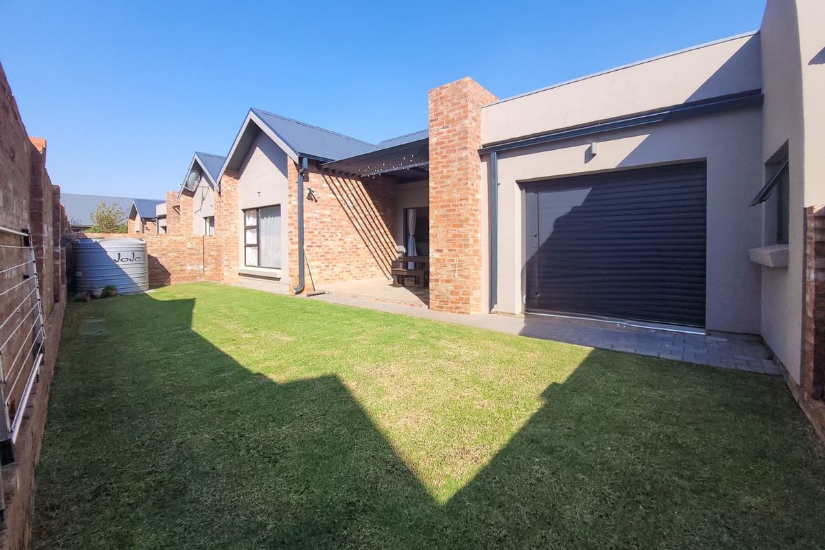 A well-maintained rear exterior view of the townhouse featuring a private garden, brick facade, covered patio area, and a secure garage.