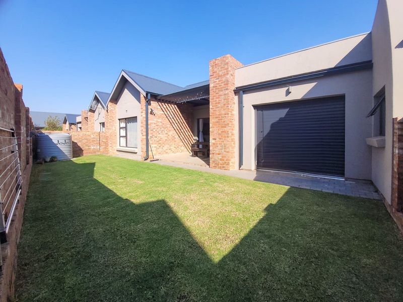 A well-maintained rear exterior view of the townhouse featuring a private garden, brick facade, covered patio area, and a secure garage.