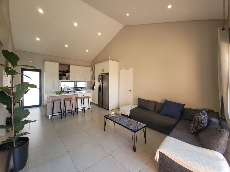 Spacious open-plan living area featuring a modern kitchen with island, vaulted ceilings, recessed lighting, and neutral tiled flooring throughout.