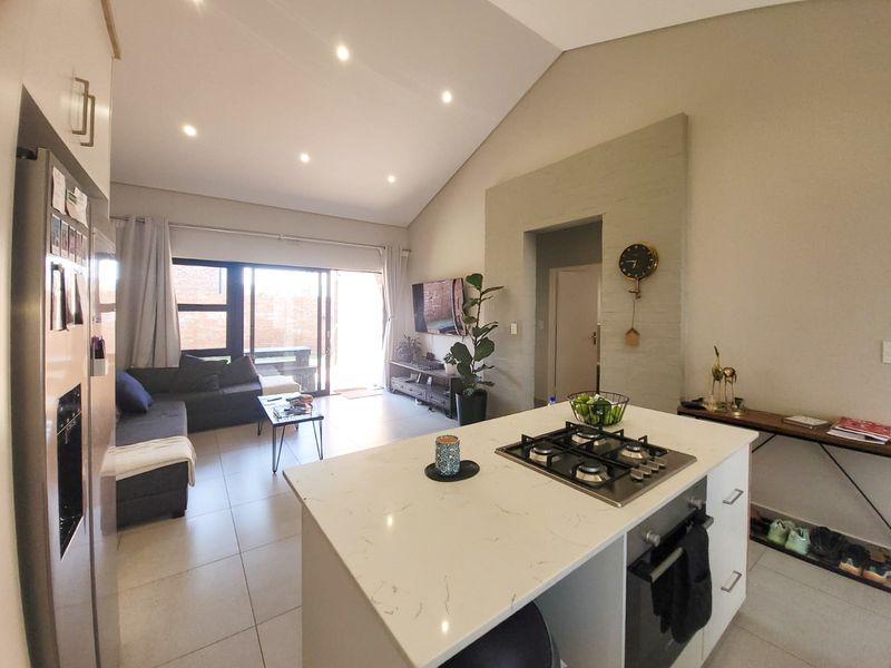 Modern open-plan living area featuring a kitchen island with gas hob, vaulted ceilings, recessed lighting, and large sliding doors leading to the patio.