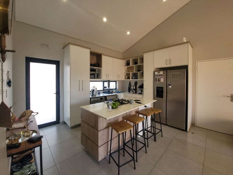 Modern kitchen featuring a central island with a gas hob, stone countertops, ample built-in cabinetry, and a high vaulted ceiling with recessed lighting.